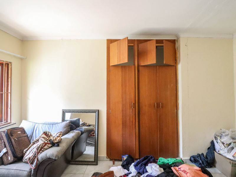 Bedroom featuring built-in wooden wardrobes and security bars on the window, showing signs of wear including cracked wall plaster and damaged cabinet doors.