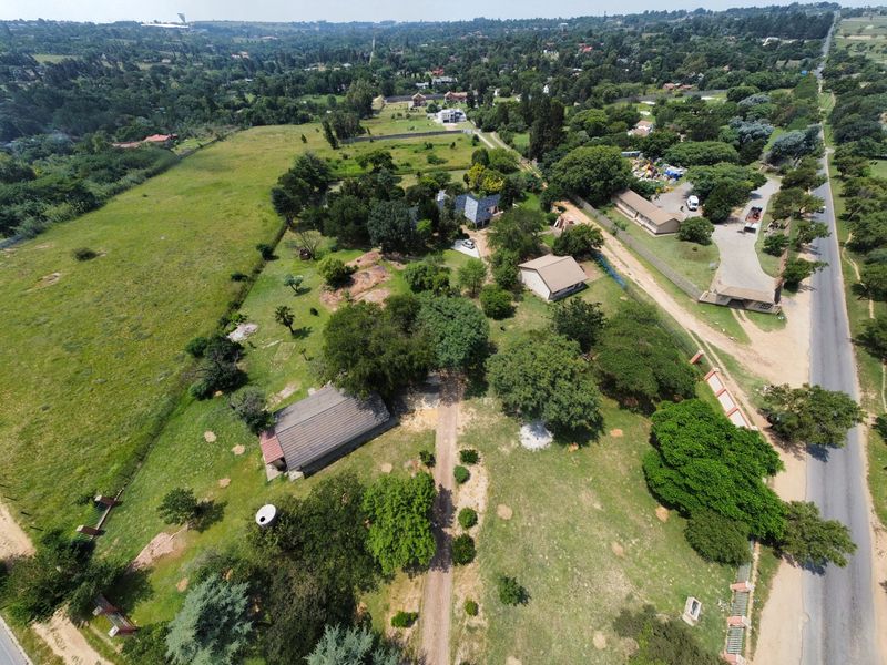 Aerial view of a small holding property featuring multiple outbuildings, expansive grounds, and established trees, with direct road access.