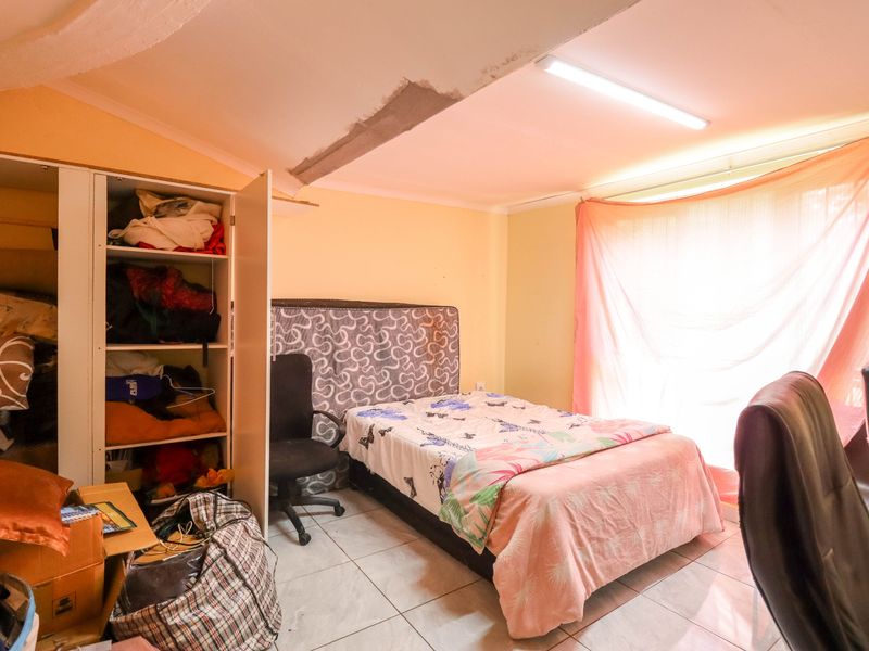 A bedroom featuring tiled flooring and a fluorescent ceiling light, currently showing signs of wear including visible ceiling plaster damage.