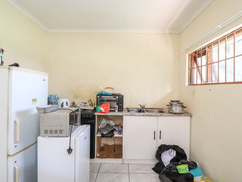 A compact kitchen area featuring basic cabinetry, a double sink, and tiled flooring, requiring cosmetic updates and maintenance to improve its overall condition.