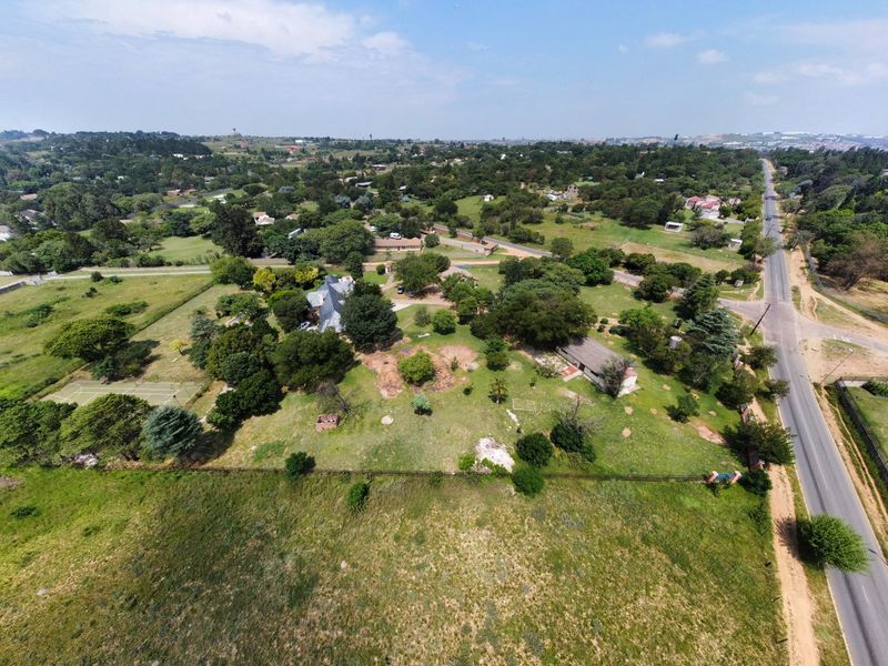 Aerial view of a spacious small holding property featuring mature landscaping, a private tennis court, and extensive grounds with direct road access.