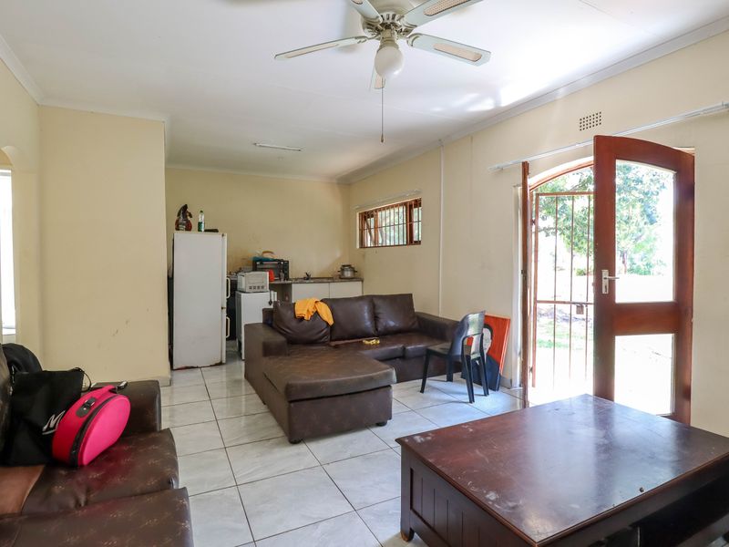 Open-plan living area featuring tiled floors, a ceiling fan, and direct access to the exterior through a security gate and wooden door.