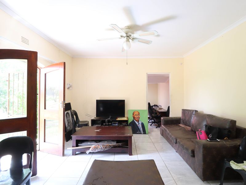 A living room featuring tiled flooring, a ceiling fan, and direct access to the exterior through a wooden door with a security gate.