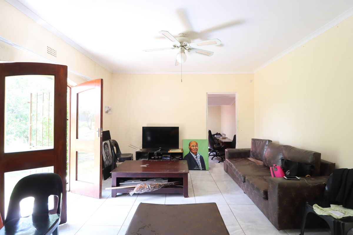 A living room featuring tiled flooring, a ceiling fan, and direct access to the exterior through a wooden door with a security gate.