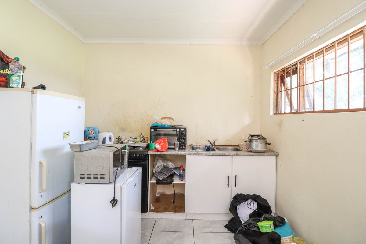 A compact kitchen area featuring basic cabinetry, a double sink, and tiled flooring, requiring cosmetic updates and maintenance to improve its overall condition.