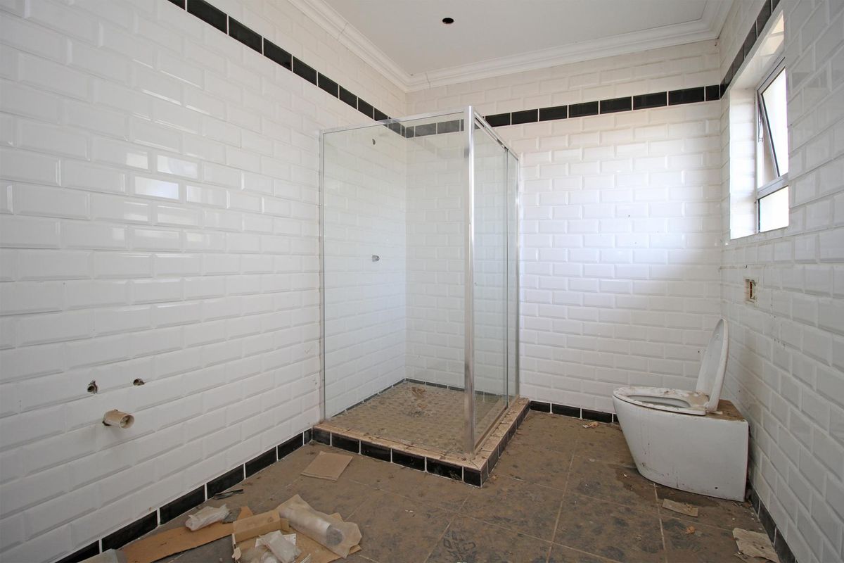 A partially finished bathroom featuring white subway wall tiles with black accents, a glass shower enclosure, and a toilet, requiring final fixtures and cleaning.
