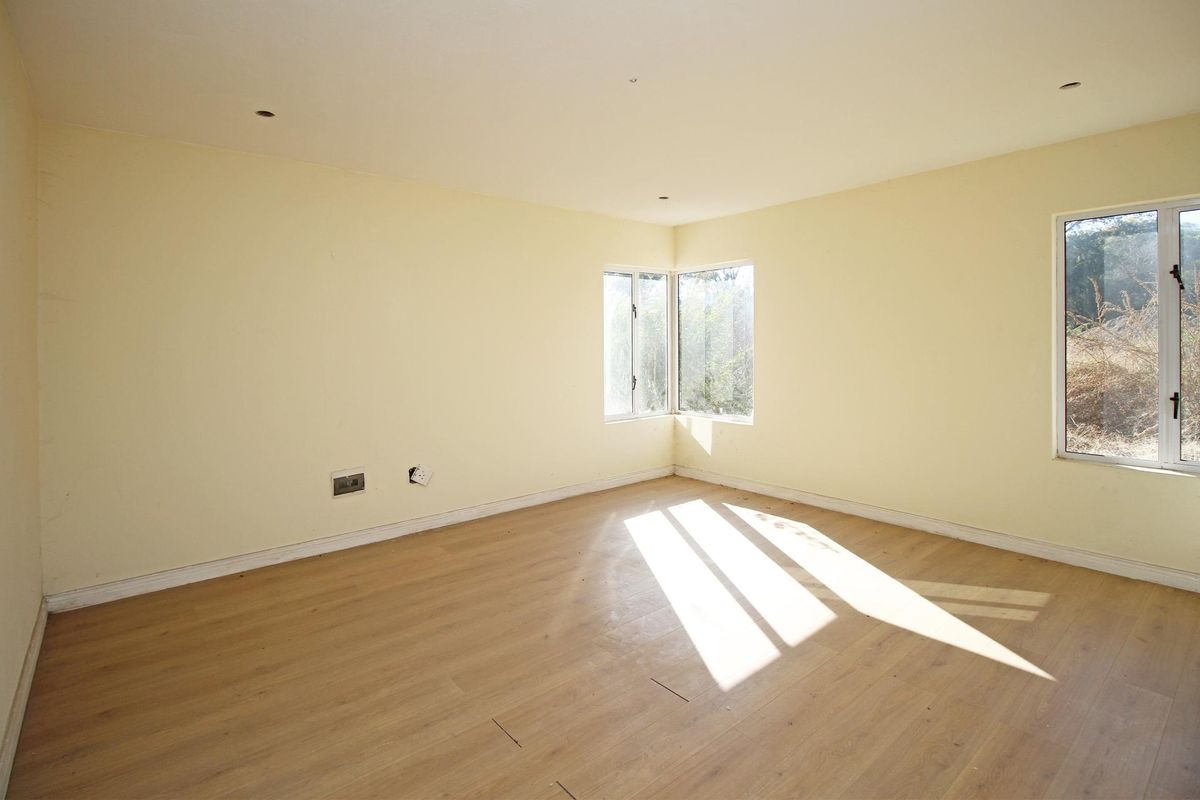 A bright, empty bedroom featuring light-toned laminate flooring, corner windows, and neutral walls, offering a blank canvas for personalization.