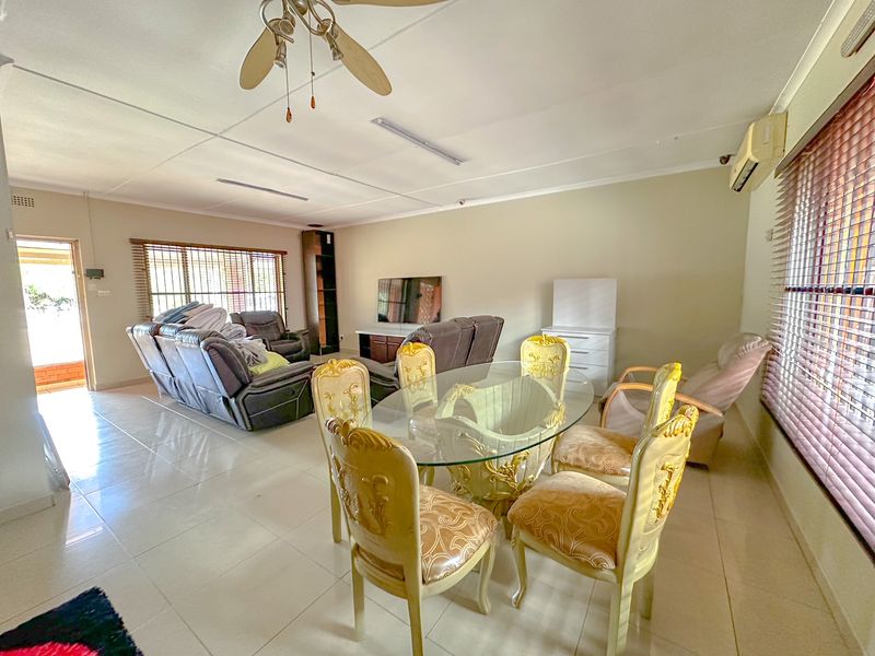 Spacious open-plan living and dining area featuring tiled flooring, a ceiling fan, and a wall-mounted air conditioning unit.