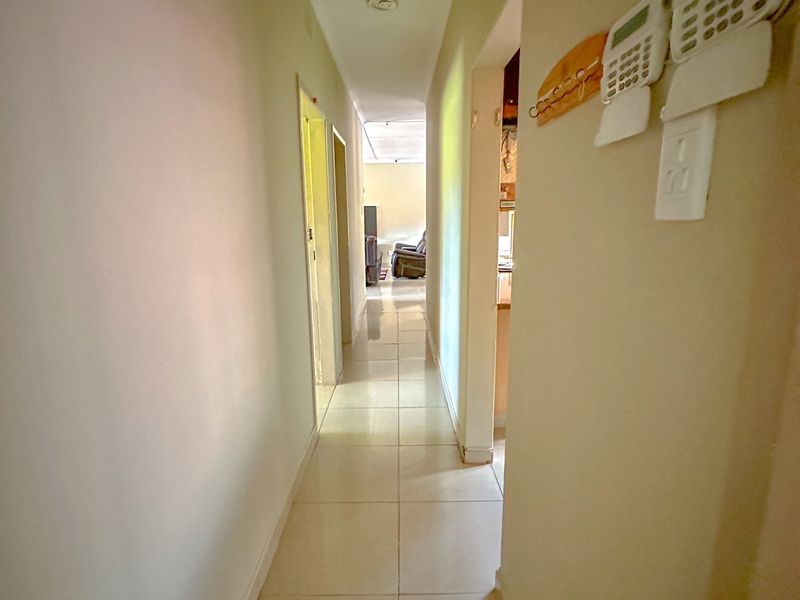 A functional hallway featuring tiled flooring and a wall-mounted security alarm system, providing access to adjacent rooms.