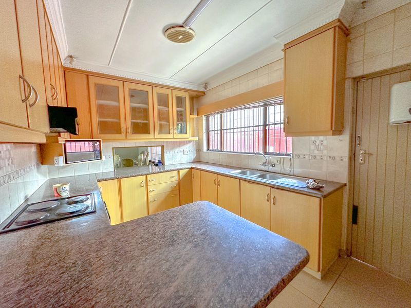 A functional kitchen featuring laminate cabinetry, granite countertops, a double basin sink, and an electric hob with an extractor fan.