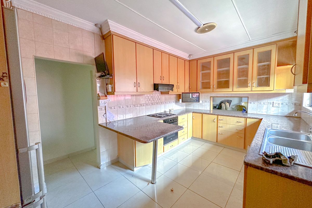 A functional kitchen featuring light wood cabinetry, granite countertops, a double basin sink, and built-in cooking appliances with tiled flooring throughout.
