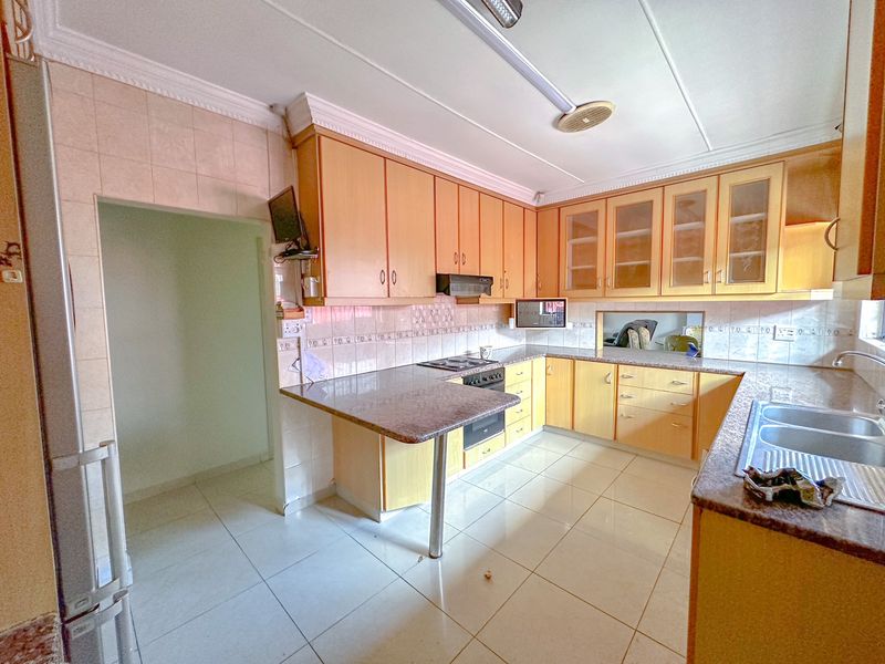 A functional kitchen featuring light wood cabinetry, granite countertops, a double basin sink, and built-in cooking appliances with tiled flooring throughout.