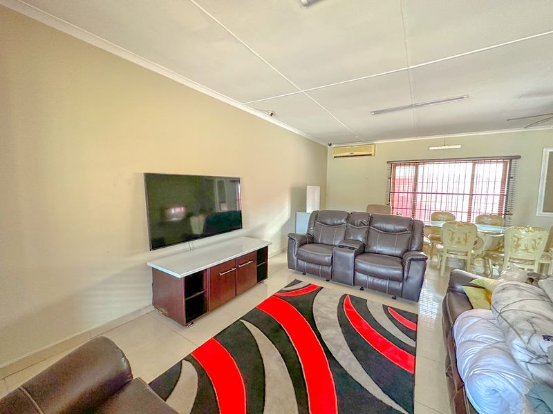 Spacious open-plan living and dining area featuring tiled flooring, split-system air conditioning, and large windows with security bars.