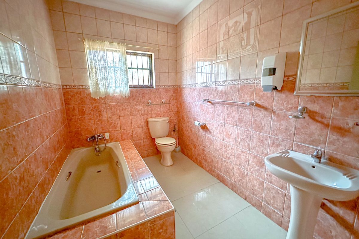 A functional bathroom featuring a built-in bathtub, pedestal basin, and toilet, finished with dated peach-toned ceramic wall tiles.