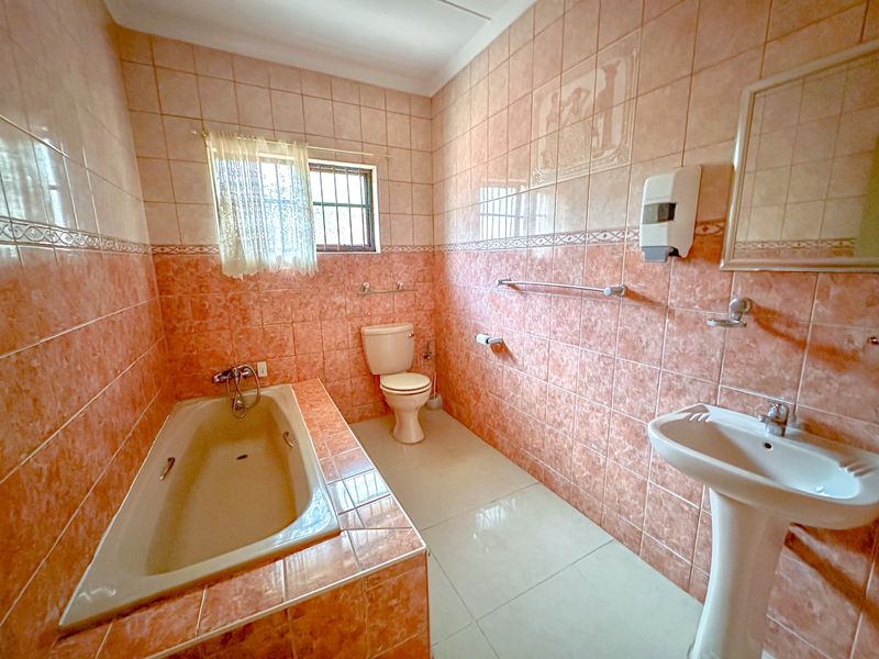 A functional bathroom featuring a built-in bathtub, pedestal basin, and toilet, finished with dated peach-toned ceramic wall tiles.