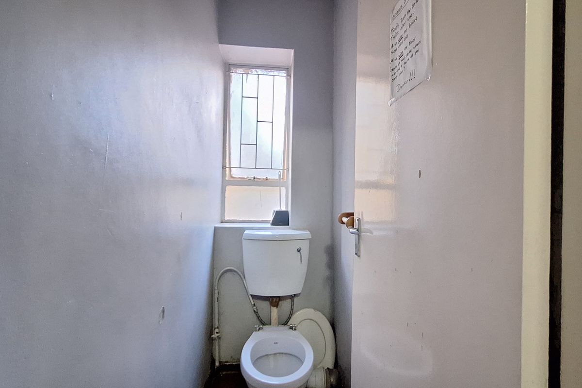 A compact, functional bathroom featuring a standard toilet and a window with security bars, requiring cosmetic updates to improve its overall condition.