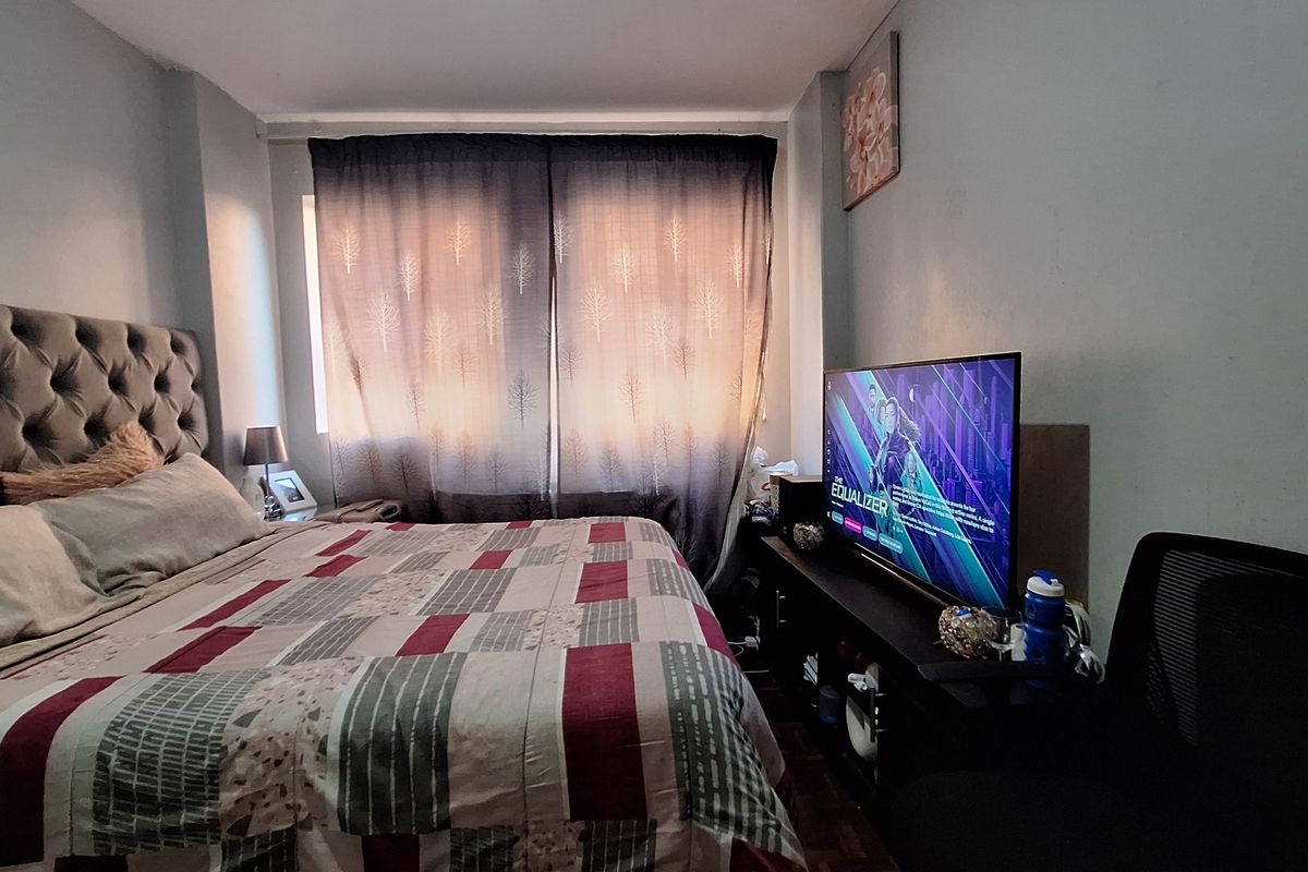 A functional bedroom featuring a window with curtains and space for a bed and media setup.