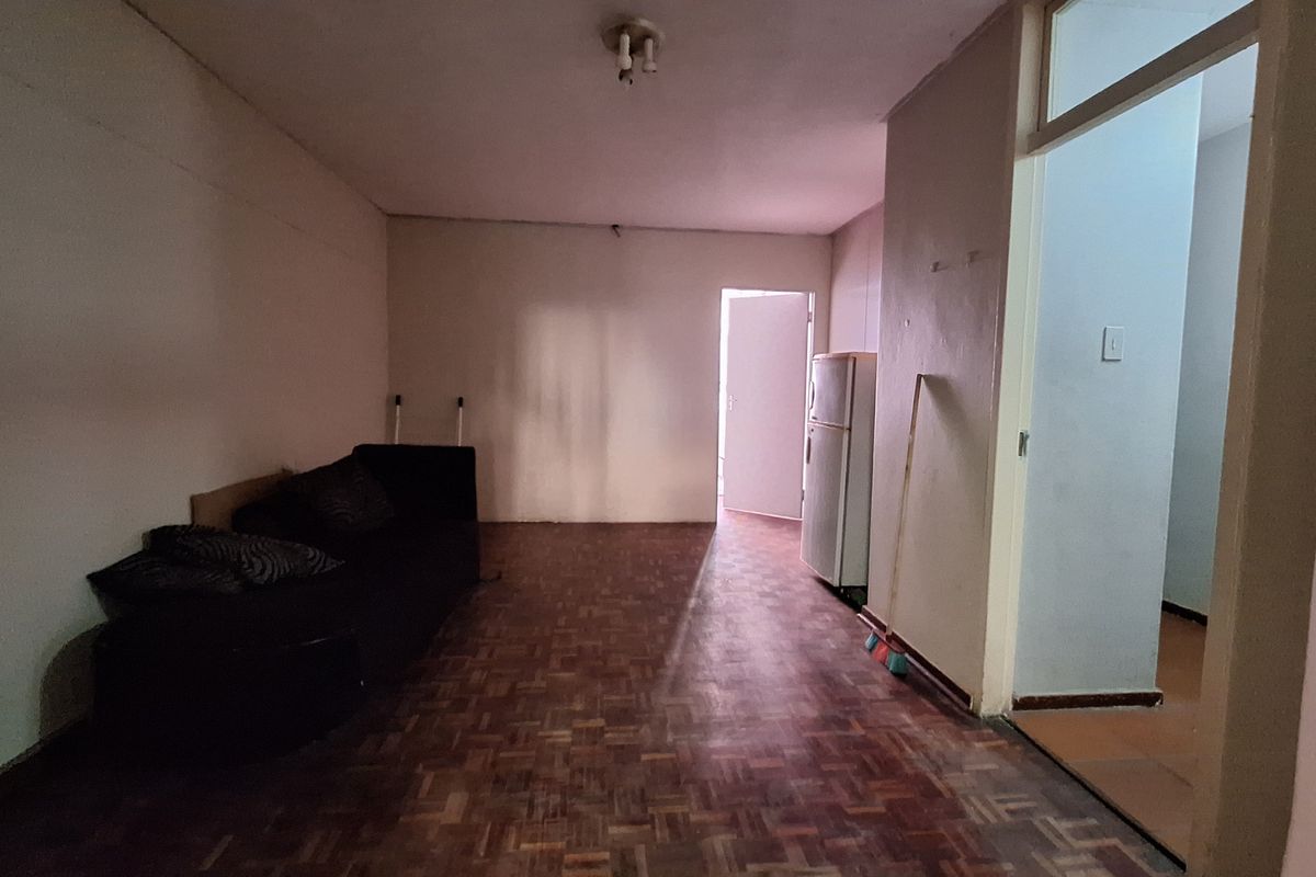 A living area featuring parquet flooring and basic lighting, requiring cosmetic updates to improve the overall aesthetic and condition of the space.