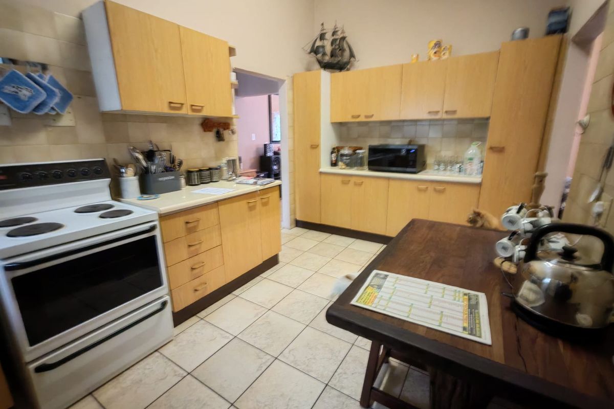 A functional kitchen featuring light wood-look cabinetry, tiled splashbacks, ceramic floor tiles, and a freestanding electric stove.