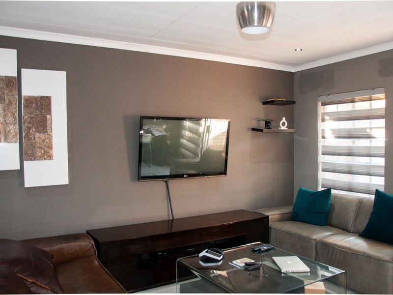 A cozy living room featuring a wall-mounted television, built-in floating shelves, and modern window blinds.