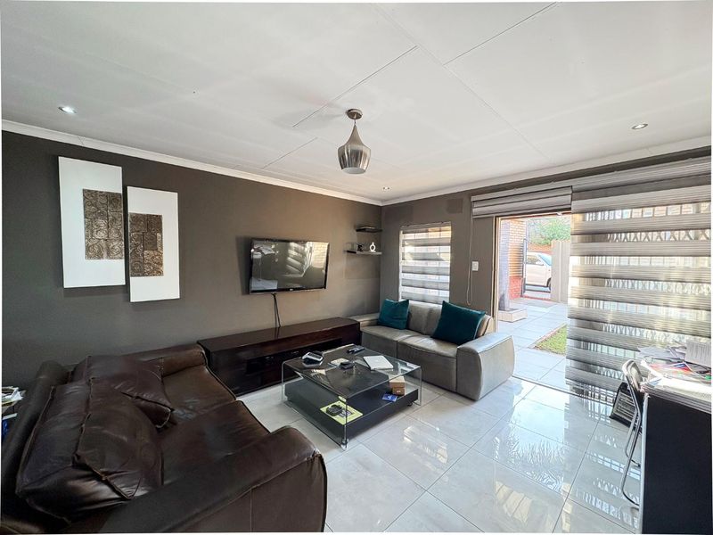 A modern living room featuring large format floor tiles, recessed downlighting, and a sliding glass door providing direct access to the exterior patio area.