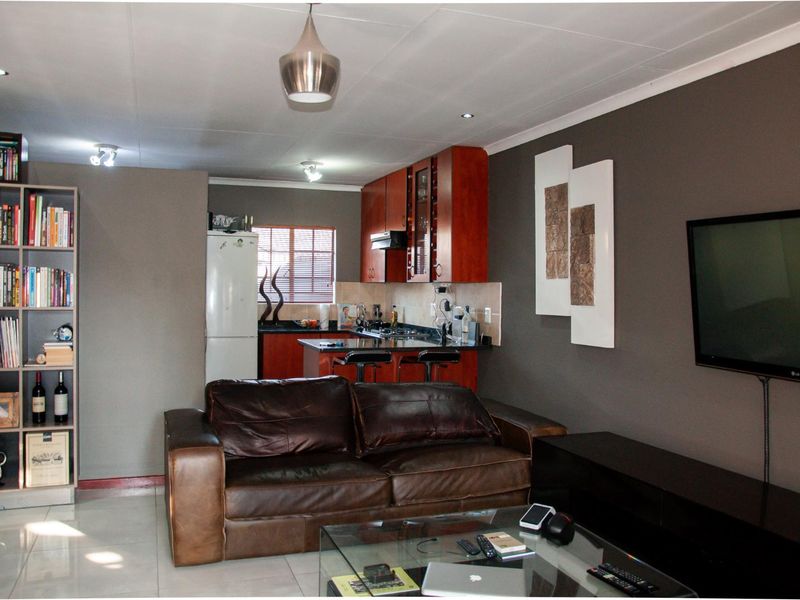 Open-plan living area featuring a compact kitchen with dark cabinetry, tiled flooring, and recessed lighting, seamlessly connected to the main lounge space.
