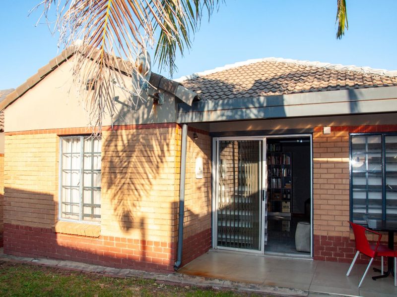 Rear view of a townhouse featuring a tiled roof, brick facade, sliding glass door with security gate, and a paved patio area.