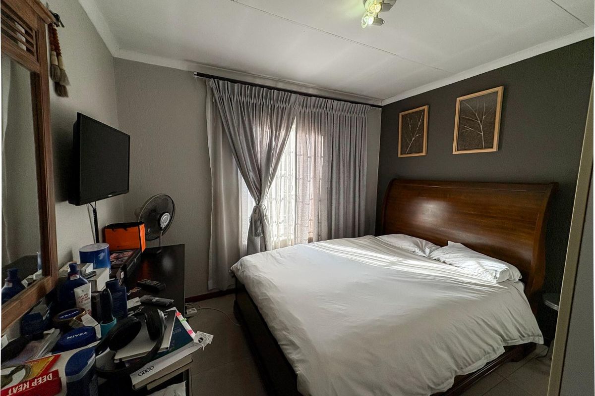 A comfortable bedroom featuring tiled flooring, a feature wall, and a window with curtain treatments, providing a functional and well-lit sleeping space.