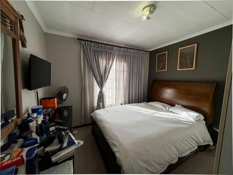 A comfortable bedroom featuring tiled flooring, a feature wall, and a window with curtain treatments, providing a functional and well-lit sleeping space.