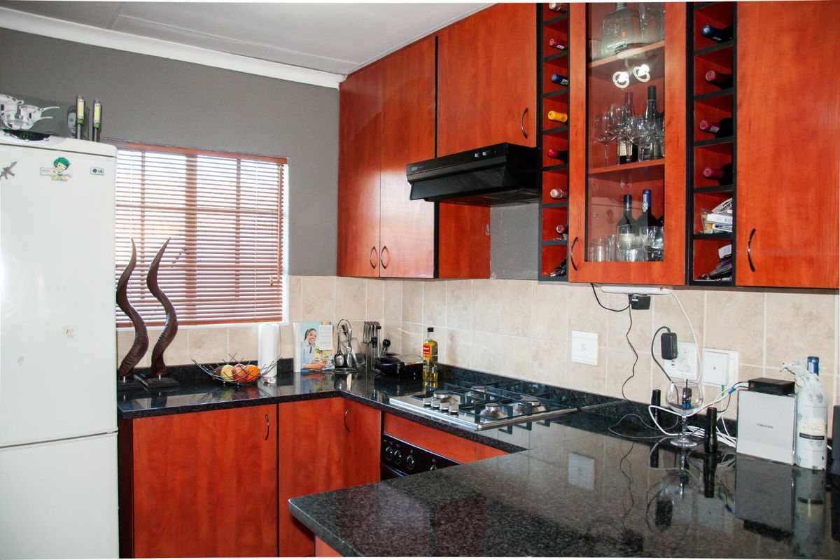 A functional kitchen featuring dark granite countertops, wood-veneer cabinetry, a built-in gas hob, and an integrated extractor fan.