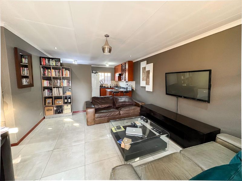 Open-plan living area featuring tiled flooring, neutral wall tones, and a compact kitchen with wooden cabinetry and integrated appliances.