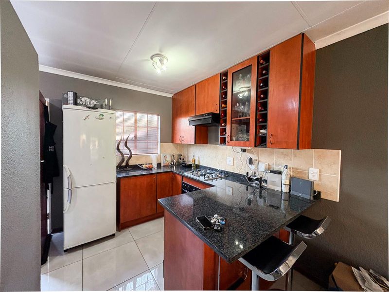A functional kitchen featuring wood-finish cabinetry, granite countertops, a built-in gas hob, extractor fan, and a breakfast bar counter.