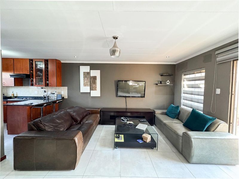 Open-plan living area featuring a kitchen with dark cabinetry and granite countertops, flowing into a comfortable lounge space with tiled flooring.