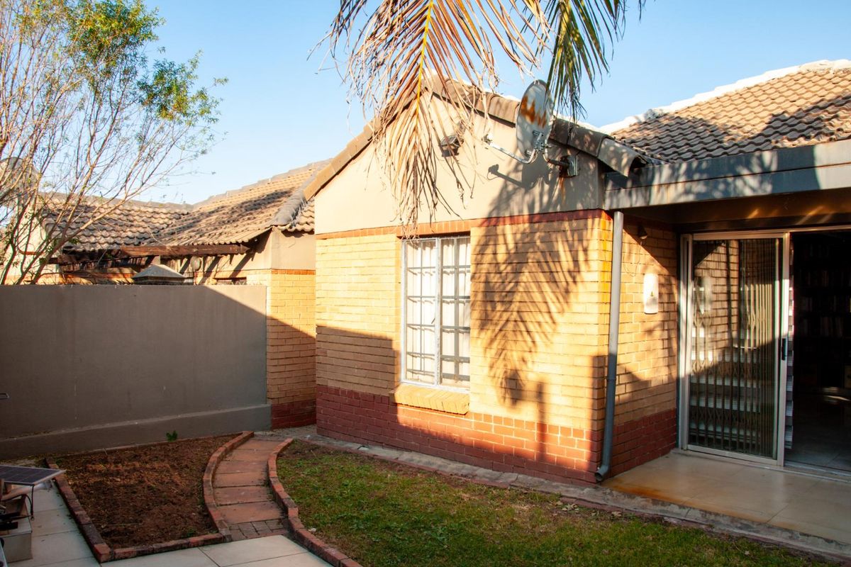 A view of the rear exterior of the townhouse, featuring a brick facade, a small garden area with a paved path, and a sliding glass door.