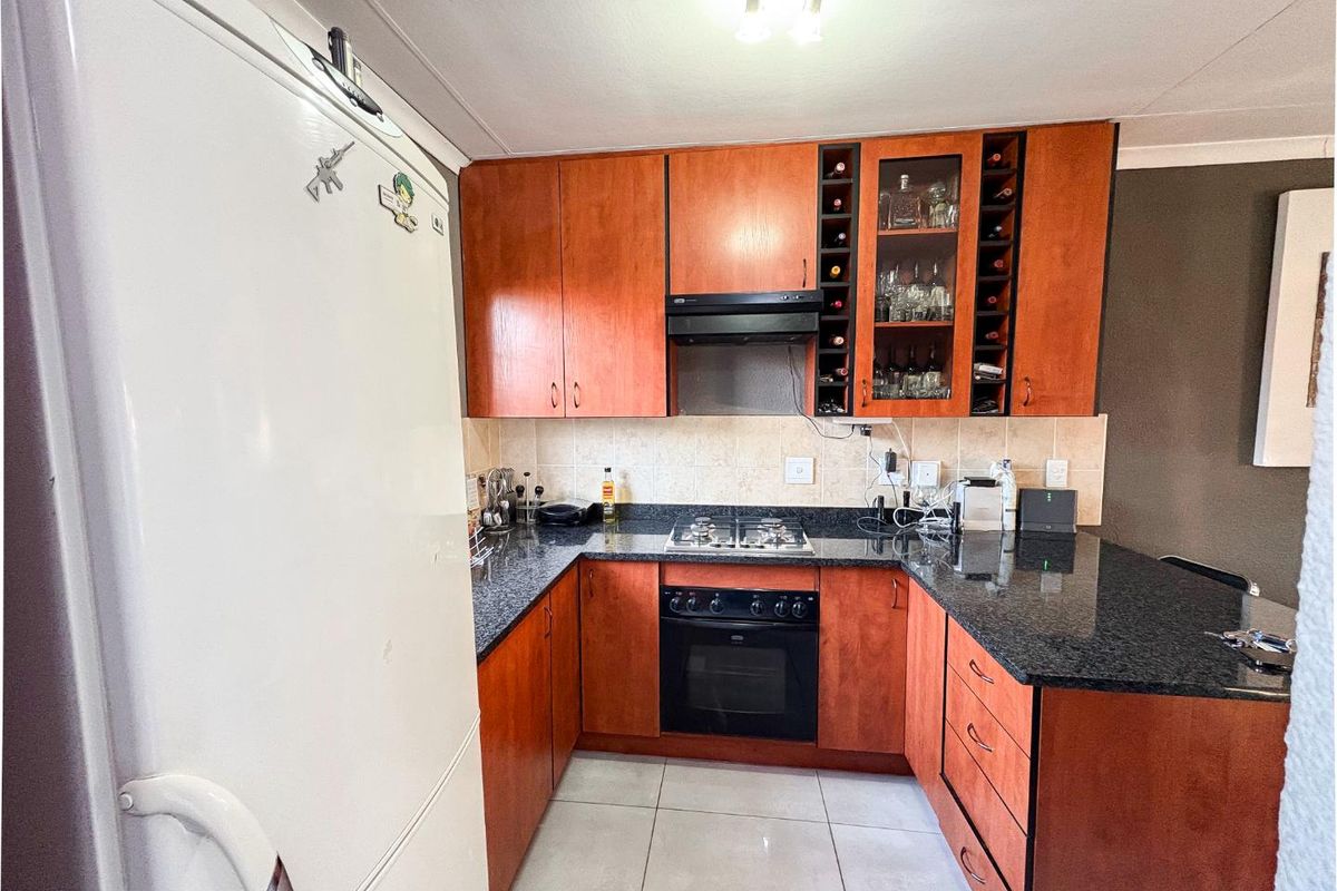 A functional kitchen featuring wood-veneer cabinetry, granite countertops, a built-in oven, gas hob, and an integrated extractor fan.