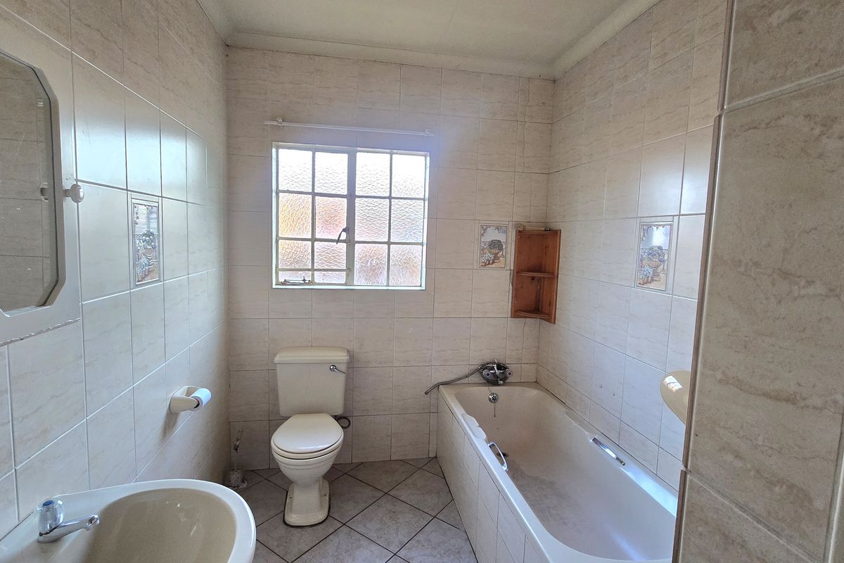 A functional bathroom featuring a bathtub, pedestal basin, and toilet, finished with neutral ceramic wall and floor tiles.