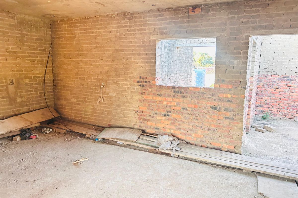 An unfinished interior space featuring exposed brick walls and concrete flooring, currently in a shell condition awaiting renovation and final finishes.