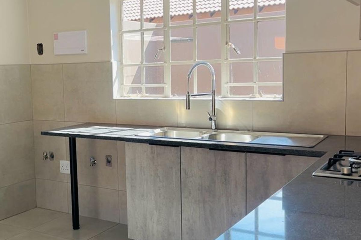 A clean, modern kitchen featuring stone-look countertops, a double sink with a gooseneck tap, and a built-in gas hob with tiled splashbacks.