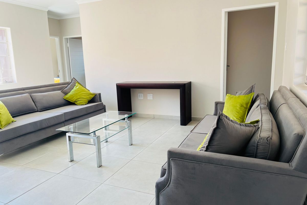 A bright and spacious living room featuring neutral tiled flooring, coved ceilings, and recessed downlighting, offering a clean and modern aesthetic.