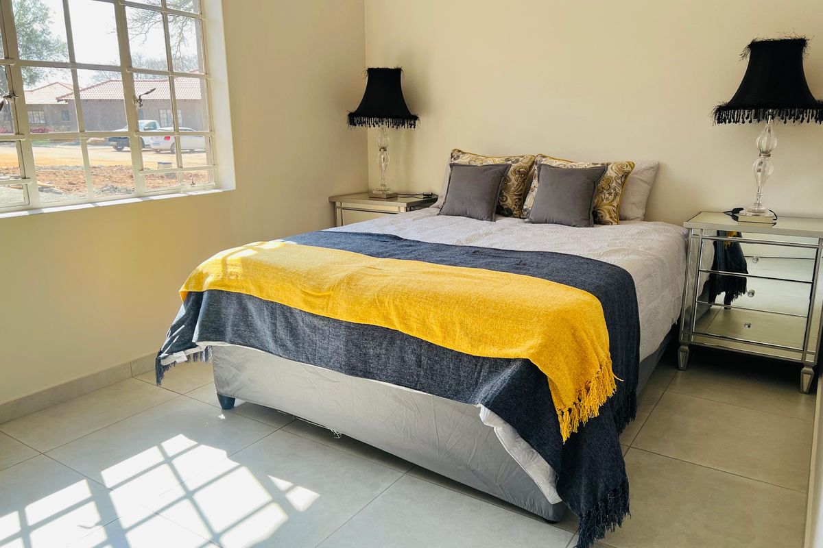A bright bedroom featuring neutral tiled flooring and a large window allowing for ample natural light.