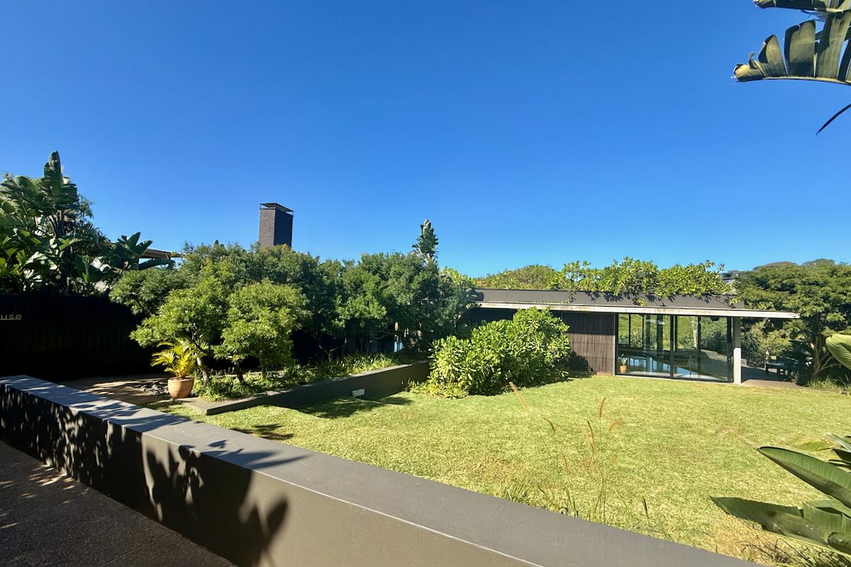 A well-maintained rear garden featuring a manicured lawn, modern retaining walls, and a contemporary building facade with large sliding glass doors.