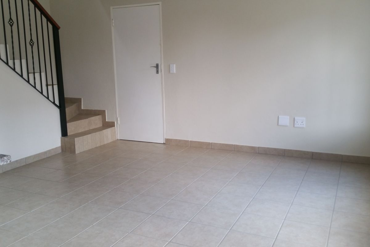 An open-plan living area featuring neutral floor tiles, a staircase with a metal balustrade, and a built-in door leading to additional space.
