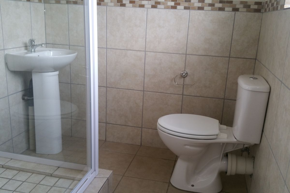 A functional bathroom featuring a pedestal basin, a glass-enclosed shower, and a standard toilet with neutral wall and floor tiling.