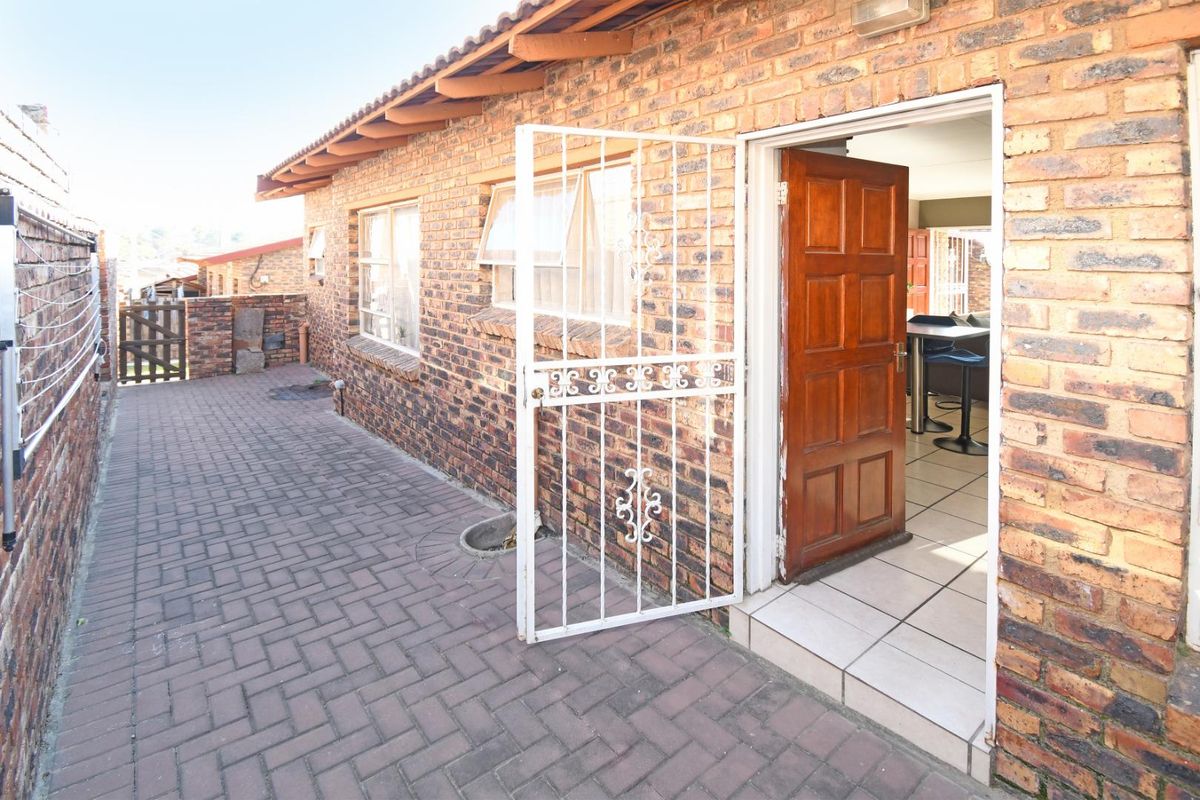 Exterior view of a townhouse featuring a paved patio area, brick facade, and a secure metal gate leading into the interior living space.