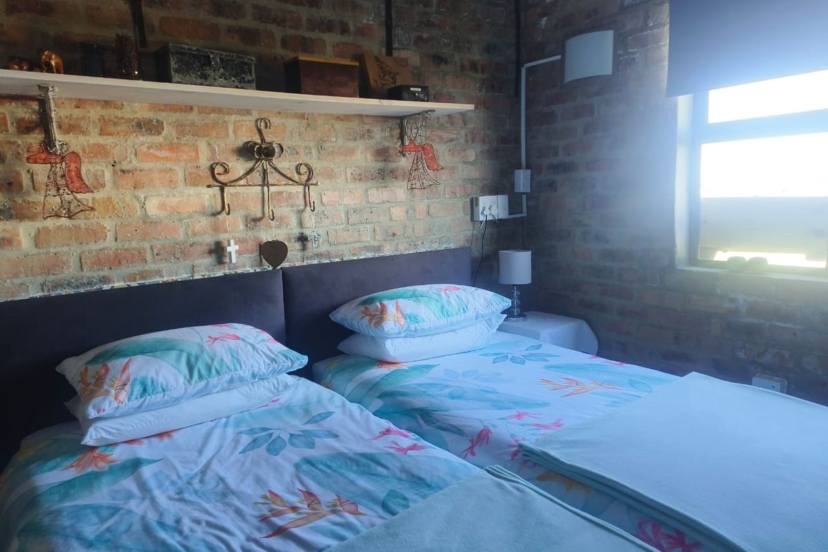 A bedroom featuring an exposed brick feature wall, built-in shelving, and natural light from a side window.