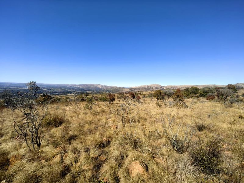 A wide-angle view of the vacant residential land featuring natural dry grass, scattered indigenous shrubs, and distant mountain range vistas.