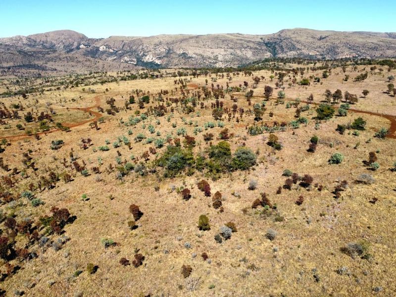 An aerial view of expansive vacant residential land featuring natural terrain, native vegetation, and existing dirt access tracks with mountain views in the distance.