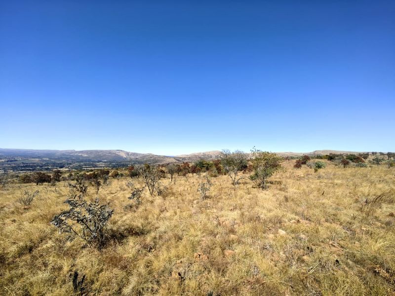 A scenic view of the natural landscape featuring dry grassland and distant mountain ranges under a clear blue sky.