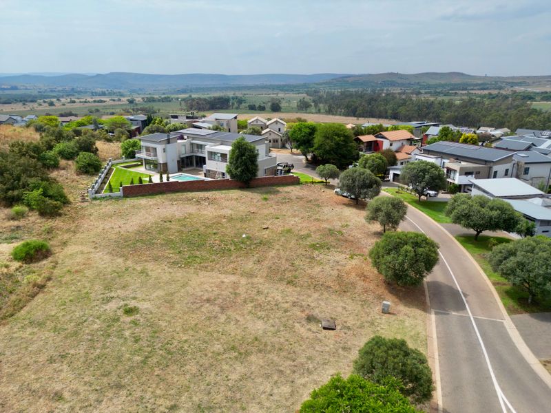 An aerial view of a vacant residential plot situated within a developed estate, featuring surrounding greenery and established neighborhood infrastructure.