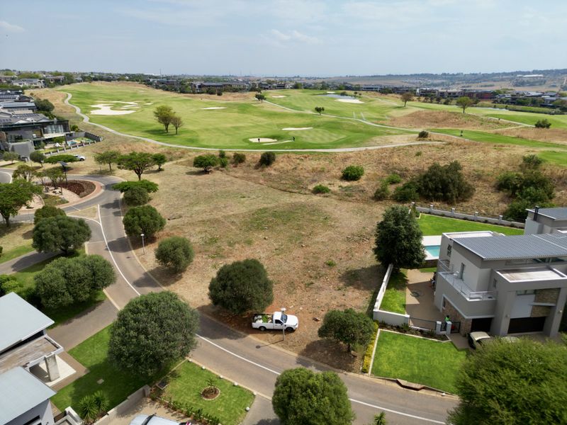 Aerial view of a vacant residential plot situated adjacent to a golf course, featuring established road access and surrounding landscaped greenery.
